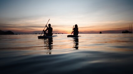 Fototapeta premium Couple paddleboarding during tropical sunset, enjoying romantic water adventure