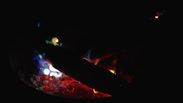 Burning embers and blue flame against complete night darkness, filmed in slow motion at 120fps for an artistic effect