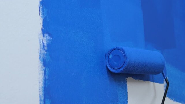 Roller Brush Painting, Worker painting on surface wall Painting apartment, renovating with blue color paint. Leave empty copy space white to write descriptive text beside.