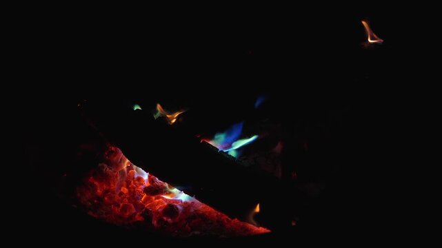 Slow burning logs with red and blue glowing flames, captured in darkness at 120fps highlighting ember texture