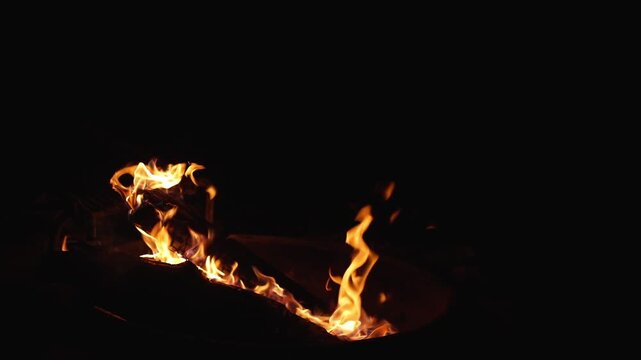 Flames slowly swaying and curling around logs at campfire, creating soft flowing motion in a slow motion frame