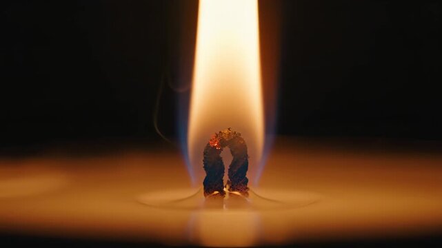 Extreme close-up of burning candle wick and flame against dark background. Glowing fire in molten wax creating warm light