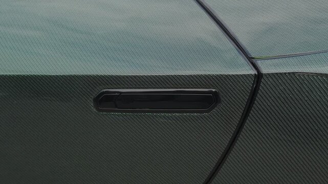 Cinematic close-up of flush door handle on carbon fiber supercar