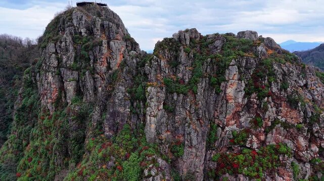 A cinematic close-up drone orbit around two sharp rock peaks in a moody autumn landscape. The camera circles the rocky formations while revealing colorful wildflowers growing on the stone surfaces, un