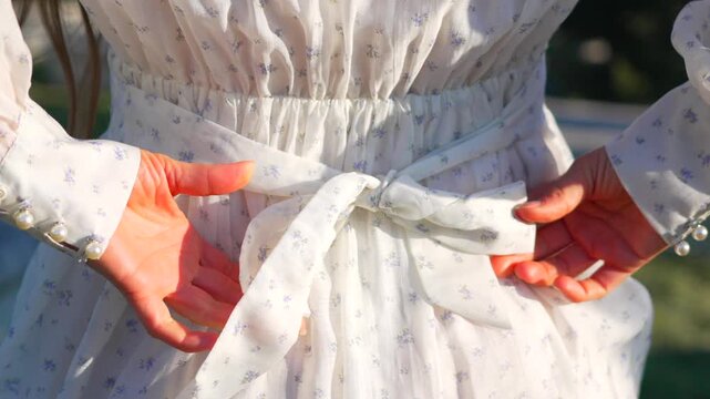 Dress bow tie woman tying floral pattern white dress belt into bow behind her back graceful getting ready moment