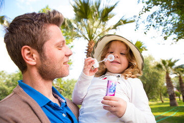 Fototapeta premium Father and daughter blowing bubbles in a tropical park