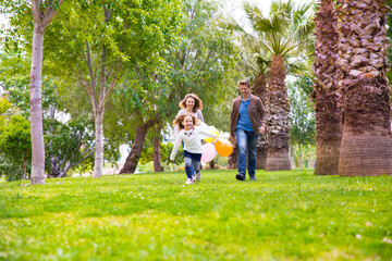 Fototapeta premium A woman and two young girls are running together in a grassy park, smiling and holding colorful balloons on a sunny day. 