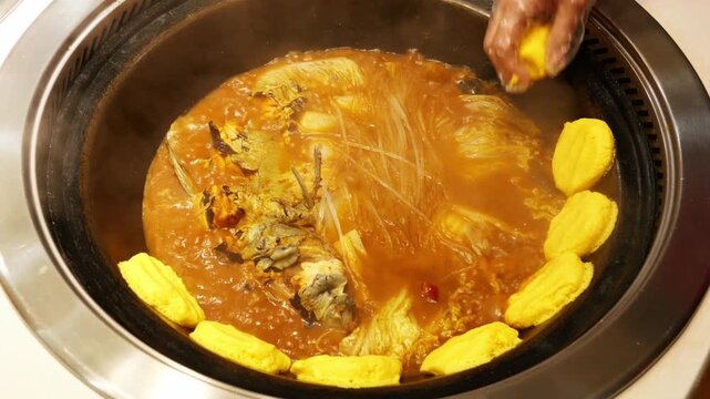 A cooked Chinese stew of fish and noodles in a cast iron wok with golden corn cakes steaming.