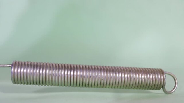 Hand pulls a flexible metal coil spring to demonstrate tension and elasticity in this high quality slow motion video clip.