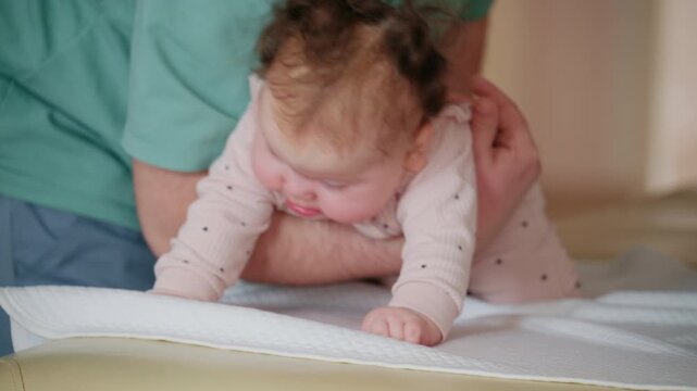 Close up view of the infant's head and upper body leaning forward, supported by an adult's forearm under the chest