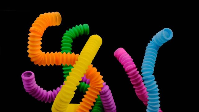 A colorful arrangement of stretchy ribbed colorful plastic flexible tubes against a black background, These are colorful plastic sensory fidget tubes designed for tactile stimulation and stress relief