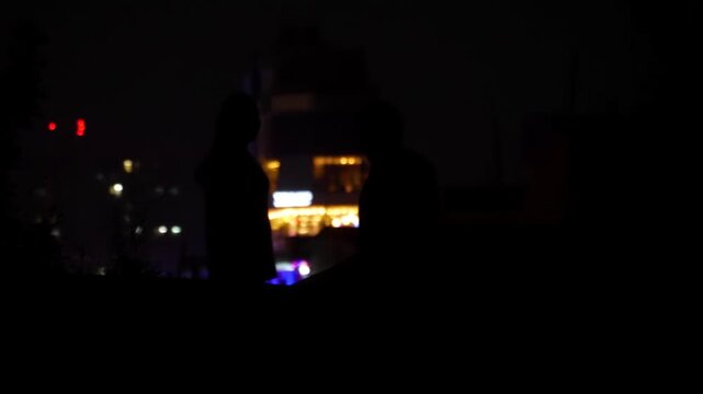 Dark Silhouette of Couple chatting and Standing Against Glowing Illuminated City Lights at Night