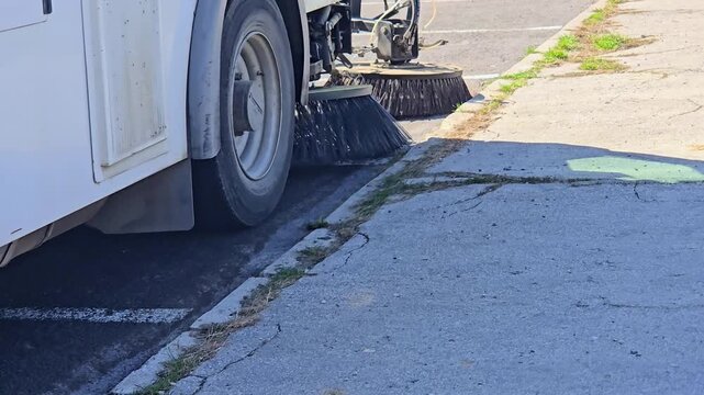 Municipal street sweeper machine cleaning asphalt road surface with rotating brushes