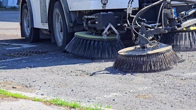 Municipal street sweeper machine cleaning asphalt road surface with rotating brushes