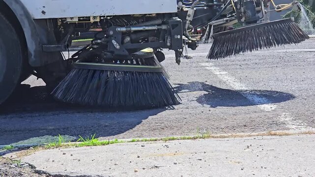 Municipal street sweeper machine cleaning asphalt road surface with rotating brushes