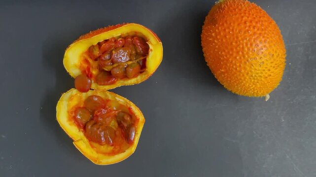 ripe orange gac fruit isolated fruit cut open on wooden board showing red seeds on dark background