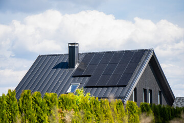 Fototapeta premium Dark wooden family home equipped with photovoltaic solar panel system on a standing seam metal roof for sustainable green energy