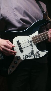 Close up view of a musician playing an electric bass guitar with a custom pickguard, skillfully plucking the strings to create a groovy rhythm during a studio session or live performance. Vertical