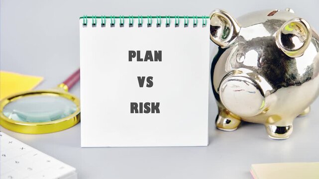 A white spiral notebook displaying Plan versus risk is positioned beside a golden piggy bank and a magnifying glass on a light grey desk, surrounded by office items