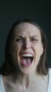 Portrait of furious woman shouting with her mouth wide open, expressing intense anger and frustration with powerful, aggressive scream and tense facial expression on a dark background. Vertical video
