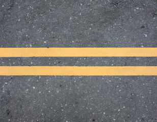 Fototapeta premium A detailed close-up view showcases a textured asphalt road surface marked with bright yellow double lines, highlighting the granular composition and the purposeful lane division.