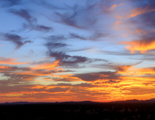 Obraz premium A vibrant sunset paints the sky with fiery orange and blue hues, contrasting with the dark silhouette of distant mountains.