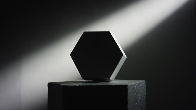 Geometric hexagonal object transitions from a two-tone design to a solid black appearance, illuminated by a beam of light against a dark background on a textured surface