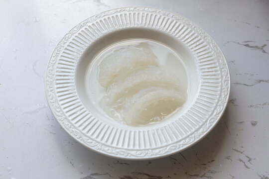 Raw edible bird's nests soaking in a bowl of water on a white marble background. Traditional Chinese health delicacy.