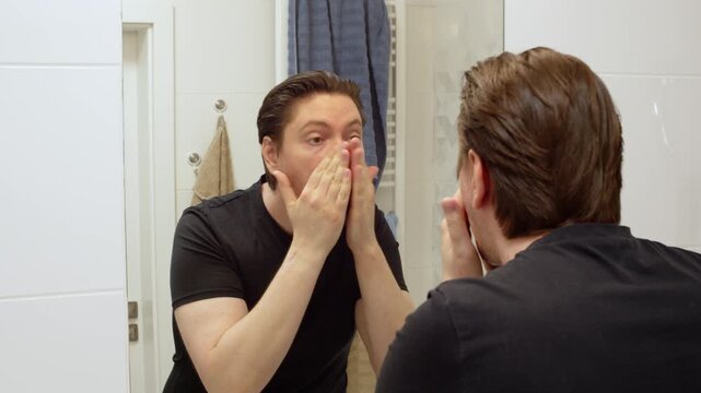 Average man applying and intensely massaging face cream into his skin in the bathroom
