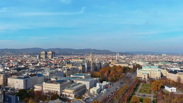 4K aerial view of Vienna's Ringstrasse with Rathaus city hall, Austrian Parliament, Burgtheater and Votivkirche surrounded by autumn foliage and Vienna Woods.