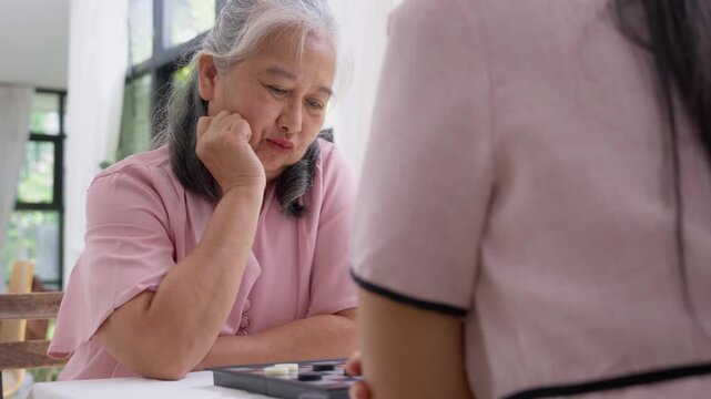 Intergenerational Play: Capture a tender moment as an elder and her granddaughter engage in a board game, the soft light and gentle gestures convey warmth and the bond between generations.