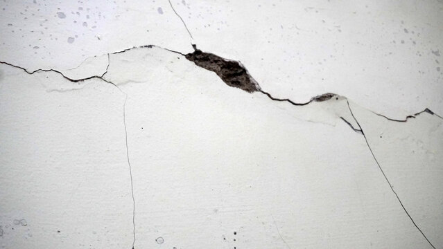 Severely cracked white wall with deep fractures and exposed interior damage. Dramatic structural defect texture ideal for earthquake, decay, and construction damage themes.