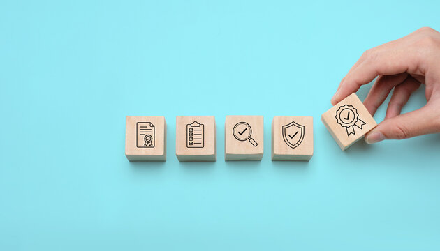 Quality certification concept with wooden blocks showing document checklist inspection shield and award badge icons representing quality assurance compliance audit and approved standards