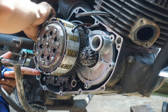 The process of manually repairing or servicing a motorcycle engine by a mechanic. The mechanic's hands are seen removing or installing a cover component near the cylinder block of a two-stroke engine.