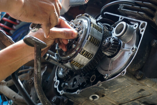The process of manually repairing or servicing a motorcycle engine by a mechanic. The mechanic's hands are seen removing or installing a cover component near the cylinder block of a two-stroke engine.