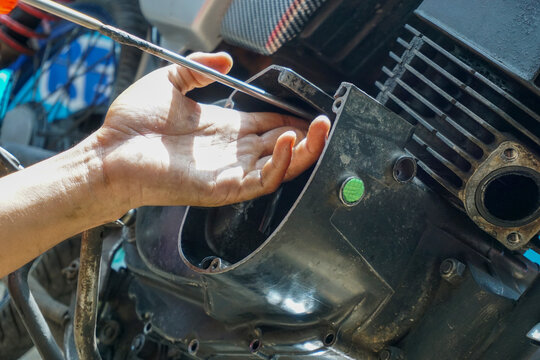 The process of manually repairing or servicing a motorcycle engine by a mechanic. The mechanic's hands are seen removing or installing a cover component near the cylinder block of a two-stroke engine.