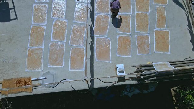 Aerial view of people sun-drying handmade food sheets on a rooftop, showing traditional rural food preparation, summer preservation, community work, and authentic daily life in a warm village setting.