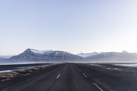 Ring road, country road by the sea, rugged volcanic landscape, mountains with snow, Iceland