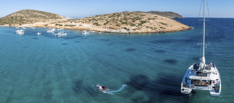 Departure by motorboat, sailing catamaran in a bay, Cyclades Island, Aegean Sea, Greece