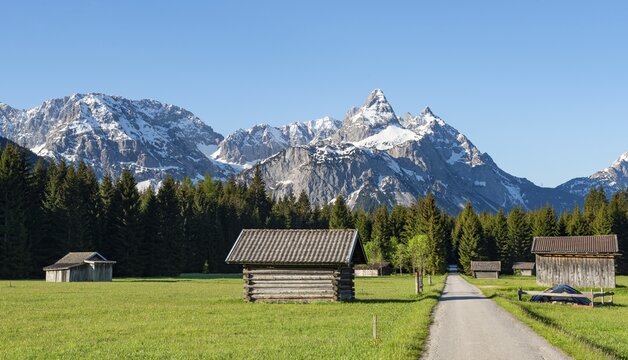 Road through meadow with hay barns, in the background snow-covered mountain peaks in spring, Mieminger Kette with Ehrwalder Sonnenspitze, Ehrwald, Tyrol, Austria