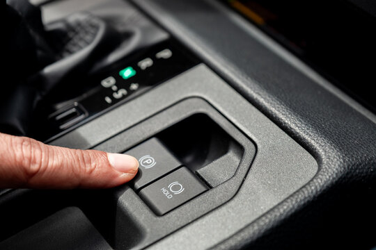 Close up of a driver's finger pressing an electronic parking brake button in a car console. Modern automatic handbrake and auto hold system concept for automotive vehicle interior