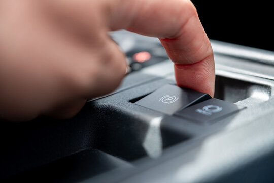 Close up of a driver pulling electronic parking brake switch on a car console panel. Modern automatic handbrake and auto hold safety system concept for commercial automotive vehicle interior