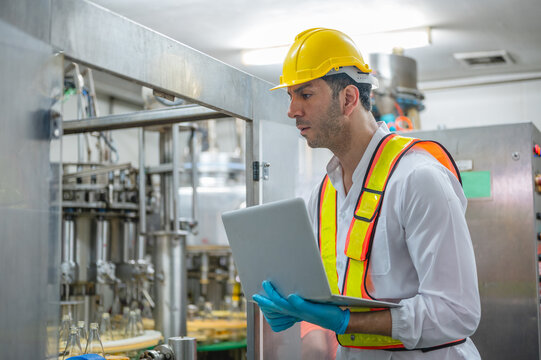 Industrial engineer inspecting beverage production line with laptop in modern factory for quality control