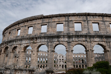Naklejka premium Exterior view of Roman arena in Pula Croatia with ancient stone arches and cloudy sky over historic landmark