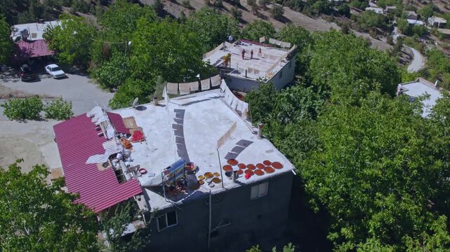 Aerial view of people sun-drying handmade food sheets on a rooftop, showing traditional rural food preparation, summer preservation, community work, and authentic daily life in a warm village setting.