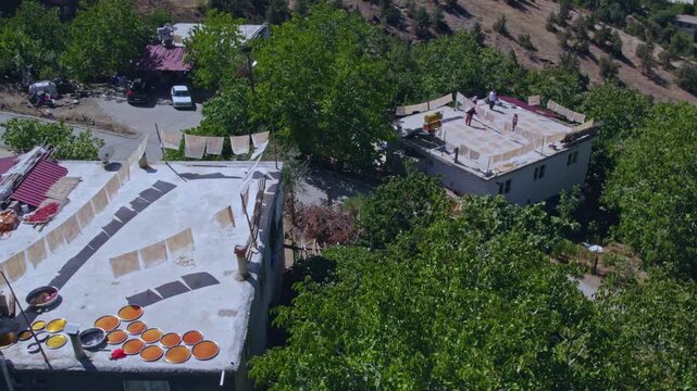 Aerial view of people sun-drying handmade food sheets on a rooftop, showing traditional rural food preparation, summer preservation, community work, and authentic daily life in a warm village setting.