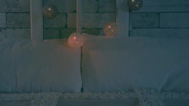 Bed with unlit decorative fairy lights in bedroom, soft beige blanket with white pillows, decorated brick wall and glowing string lights in background, cozy calm home atmosphere, Evening relaxation