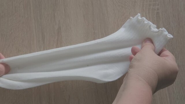 Female hands check cotton socks for quality, meticulous inspection footwear, Elastic bands and fabric texture. Diabetic-friendly apparel. Clothing purchase