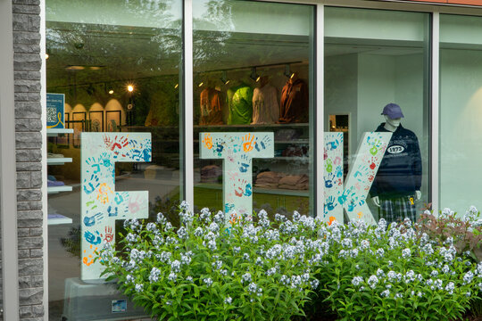 Vibrant FTK Handprint Display in Storefront Window with Mannequins, THON Merchandise, and Lush Flowering Bush in Foreground, Reflecting Greenery
