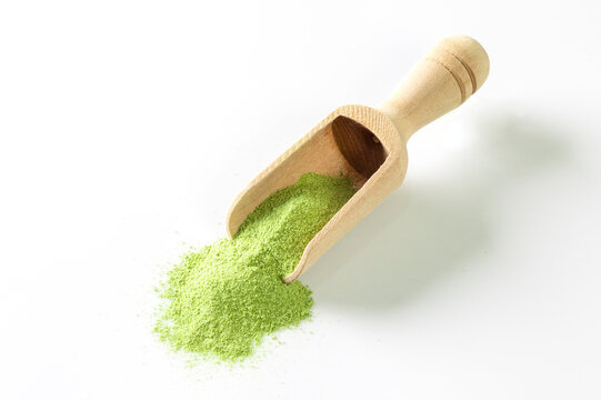 Wooden spoon with powdered matcha tea and fresh leaves on white background
